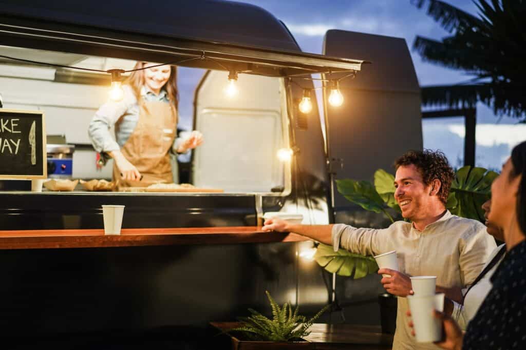 Happy people having fun drinking in counter at food truck restaurant outdoor - Focus on man face