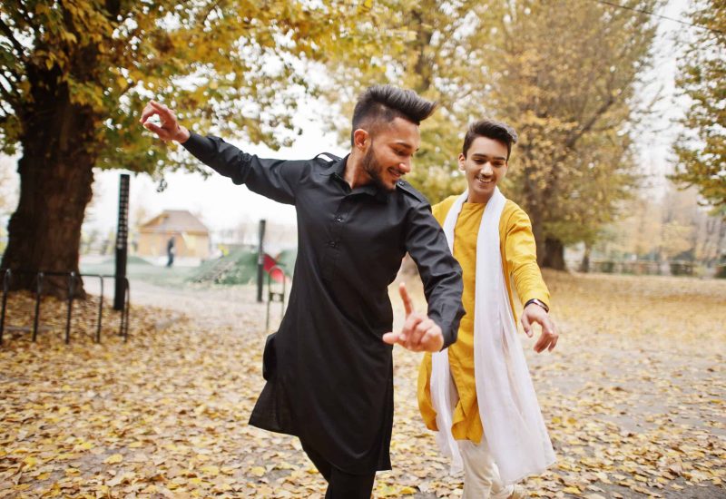 Two indian stylish mans friends in traditional clothes dancing outdoor. Navaratri dance.